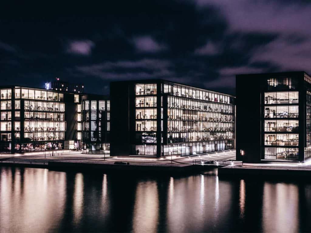 Three large commercial real estate buildings across a river a night